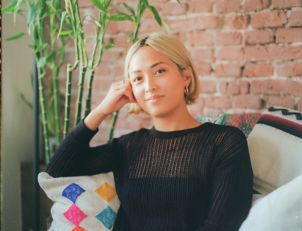 Portrait of Jamie Santiago sitting beside plants and a brick wall